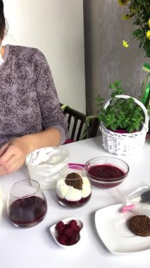 Tıbbi maskeli bir kadın pasta poşetine krema koyar. Ahududu reçelli krem peynirli tatlı pişirmek. Malzemeler masa yüzeyine serildi. Kurabiye, ahududu ve mi ile süslenmiş.