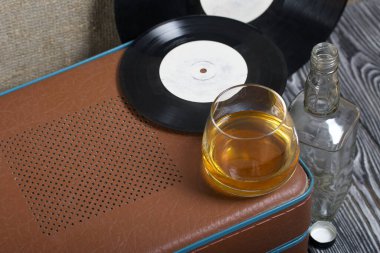 Bavul şeklinde eski bir pikap. Yakınlarda bir bardak sert alkol, boş bir cam şişe ve plak plağı var. Retro parti ekipmanları.