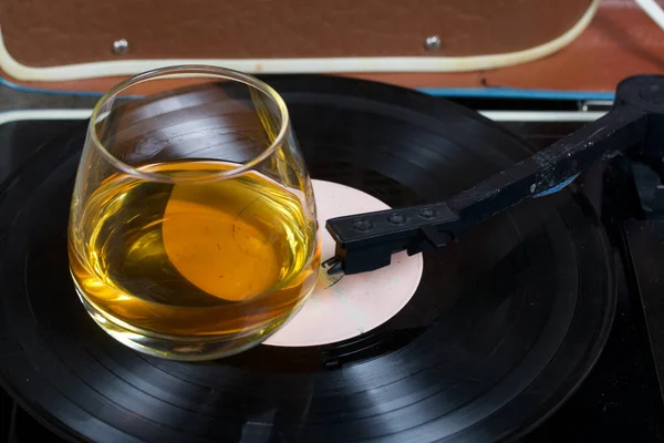 Old turntable. Nearby is a glass of strong alcohol. Retro party equipment.