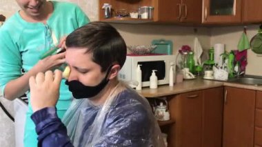 Kadın mutfakta kocasını kesiyor. Tıbbi maskeli bir koca. Evde saç kesimi, kendini soyutlama..