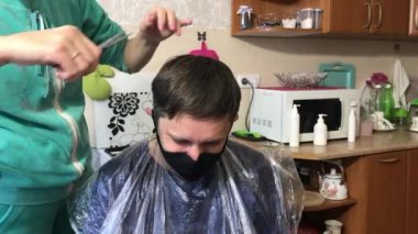 Kadın mutfakta kocasını kesiyor. Tıbbi maskeli bir koca. Kendini soyutlayarak evde saç kesimi..