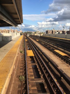Queens, New York 'ta metro istasyonundaki metro raylarına bakıyorum. Boş metro platformu. Bulutlu mavi gökyüzü. New York 'taki açık metro durağı..