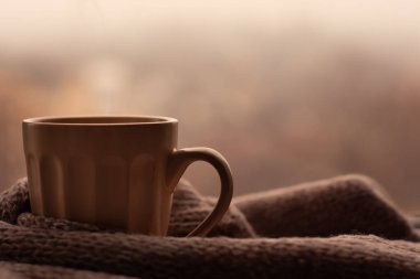 Buharlı kahve fincanı ve bulanık arka planda örülmüş süveter. Bej renkler, sonbahar kupası, sonbahar kahvesi. Metin eklemek için afiş alanı modeli.