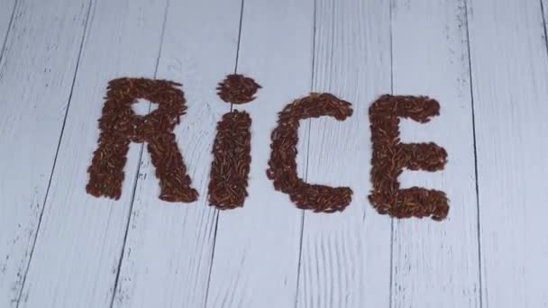 자줏빛 쌀알로 기록 된 쌀이라는 단어는 나무 배경 위에서 회전 한다. — 비디오