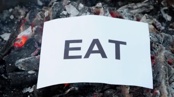 Słowo Jedz na białej kartce papieru spala się w pożarze. Zwolniony ruch — Wideo stockowe