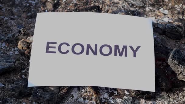 Word Economía en una hoja blanca de papel se quema en un fuego en contra. Movimiento lento — Vídeos de Stock