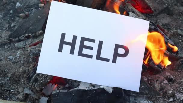 Word Help en una hoja blanca de papel se quema en un fuego contra. Movimiento lento — Vídeos de Stock