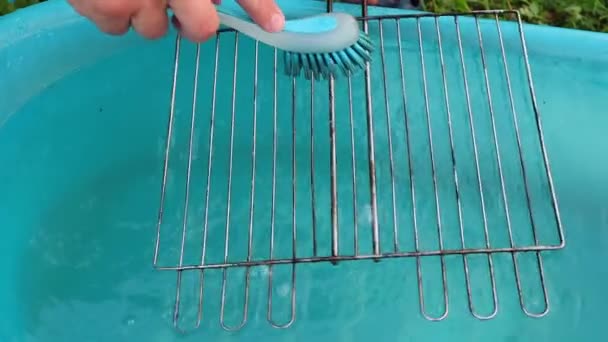 A hand with a brush washes the grill grate slowly in a blue basin — Stock Video