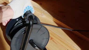 Bir işçi, ahşap zeminde duran siyah bir makaraya elektrik kablosu takar.