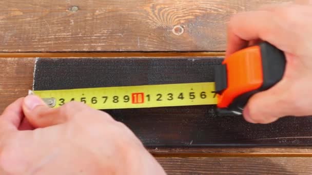 Arbeiter misst braune Planke mit Maßband auf Holzboden. FullHD — Stockvideo