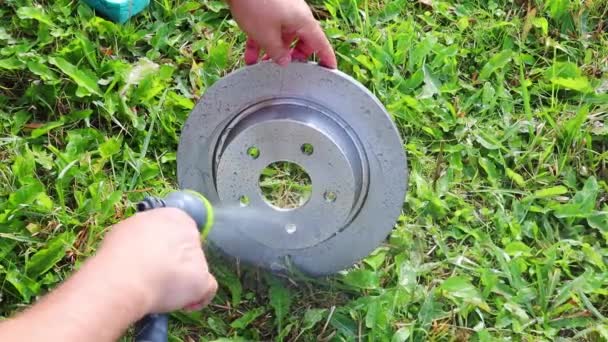 Man tvättar bil bromsskiva med vatten från en slang mot en bakgrund av gräs — Stockvideo
