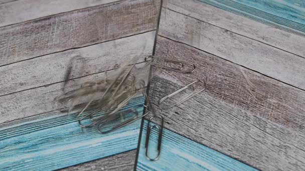 Montón de clips de papel metálicos que caen desde arriba sobre la superficie de madera de color — Vídeo de stock