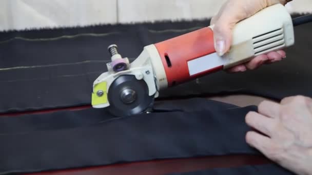 Worker cuts layers of dark tissue with electric cutter on a brown table. FullHD — Stock Video