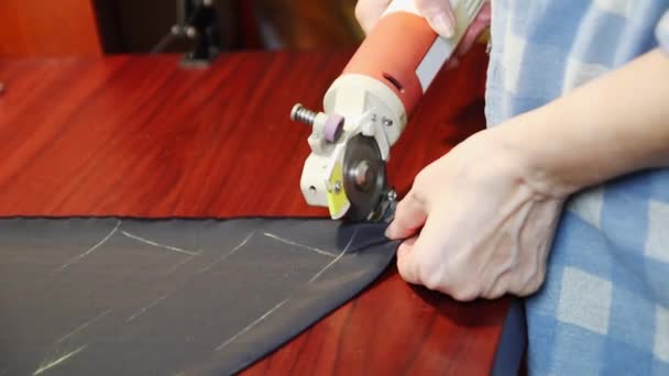 Worker cuts layers of dark tissue with electric cutter on a brown table. FullHD — Stock Video