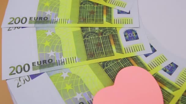 Банкноты по 200 евро вращаются на столе с разноцветными наклейками в форме сердца — стоковое видео