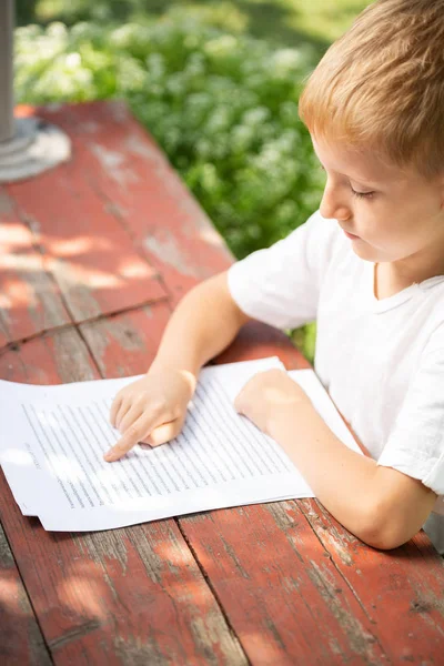 白いTシャツを着た小さな男の子が学校の概念に戻って屋外で読書しています. — ストック写真