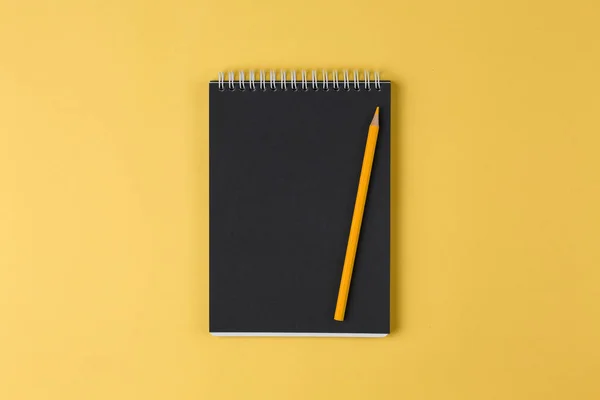 Cuaderno con papel negro y lápiz en una vista superior de fondo amarillo — Foto de Stock