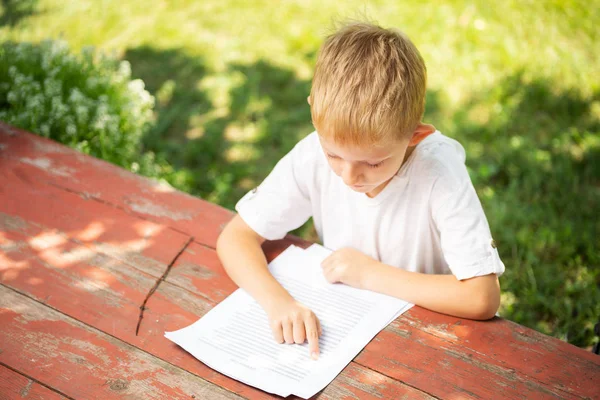 白いTシャツを着た小さな男の子が学校の概念に戻って屋外で読書しています. — ストック写真