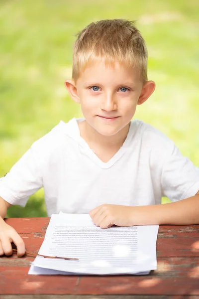 Kleine jongen in een wit T-shirt is lezen buitenshuis terug naar school concept. — Stockfoto
