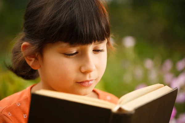 Schattig meisje leest buitenshuis op een zonnige dag, internationale alfabetiserings dag. — Stockfoto