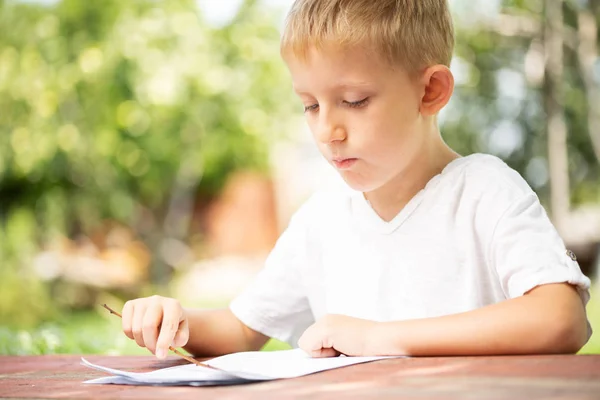 白いTシャツを着た小さな男の子が学校の概念に戻って屋外で読書しています. — ストック写真