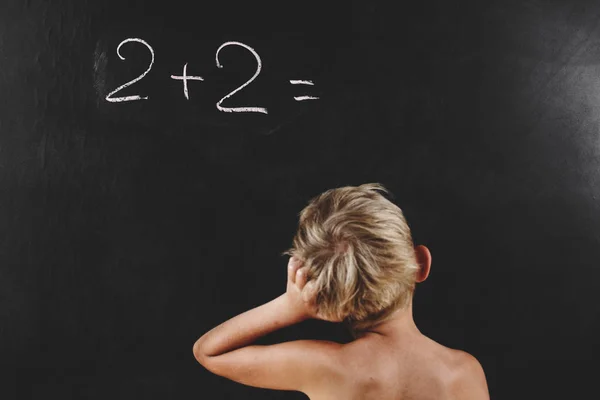 little boy without a T-shirt thinks on the blackboard