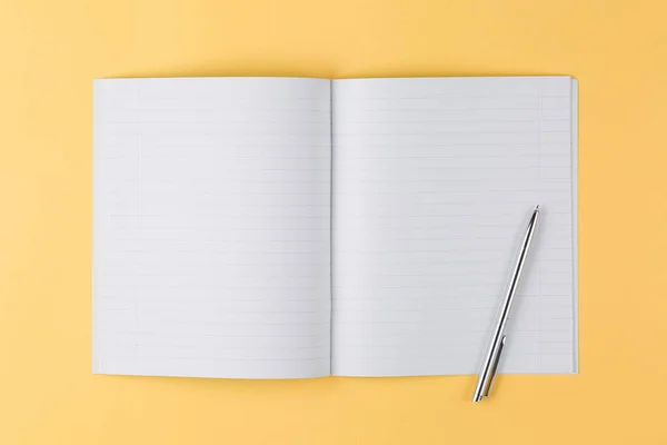 Notebook con penna nera su sfondo giallo vista dall'alto — Foto Stock