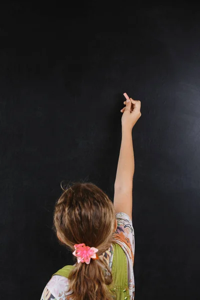 little girl is writing chalk on a blackboard