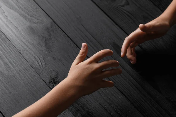 Руки вытягиваются и держат друг друга на черном деревянном фоне — стоковое фото