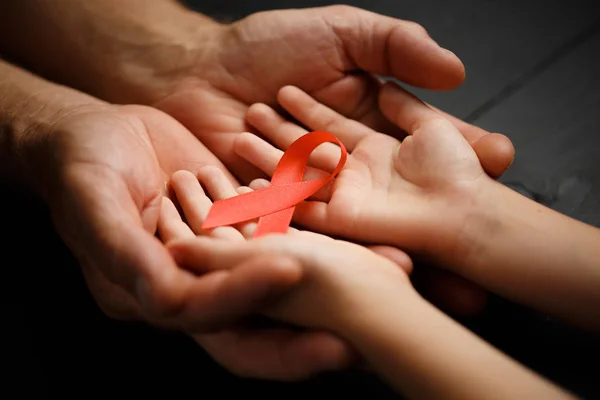 AID red ribbon in hand on a black wooden background