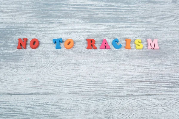 No al racismo en letras de colores sobre un fondo gris de madera —  Fotos de Stock