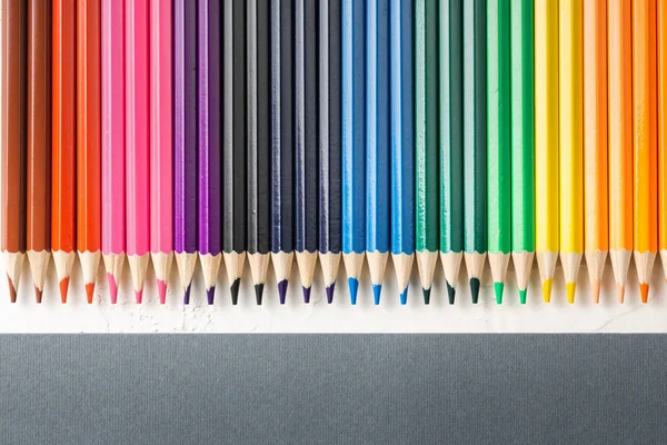 Colored pencils in row on a gray background top view. — Stock Photo, Image