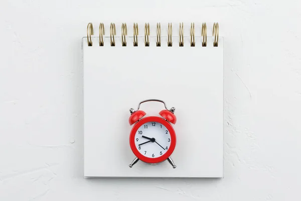 White spiral notebook with red alarm on white textured table. Flat lay mockup.