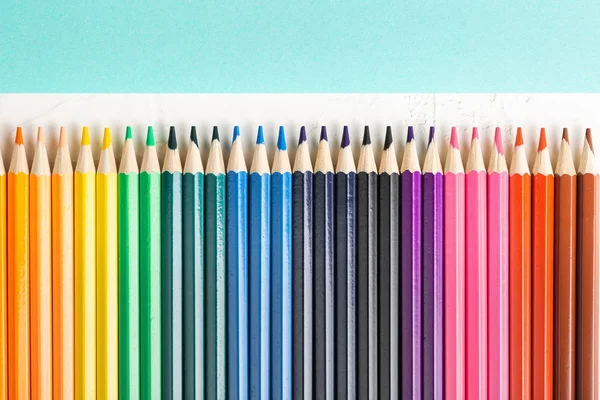 Colored pencils in row on a cyan background top view. — Stock Photo, Image