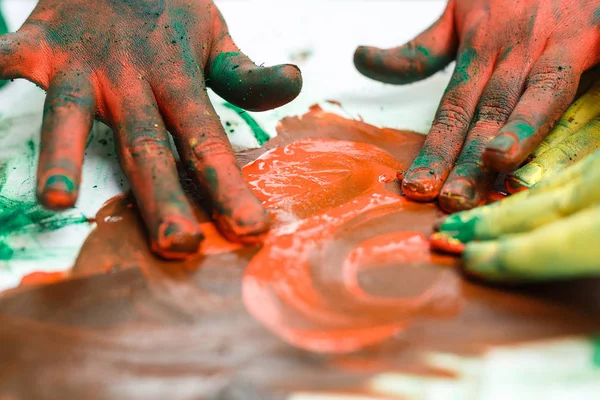 Červené ruce v barvách na pozadí lehkého stolku namalované různými barvami — Stock fotografie