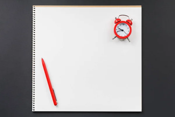 Open notebook with red alarm clock on black background — Stock Photo, Image