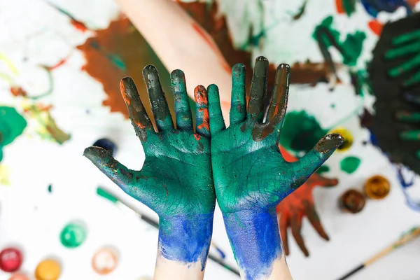 Zelené ruce v barvách na pozadí lehkého stolku namalované různými barvami — Stock fotografie
