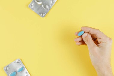 sarı arka plan üst görünümünde elinde mavi hap