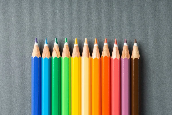 Colored pencils in row on a gray background top view. — Stock Photo, Image