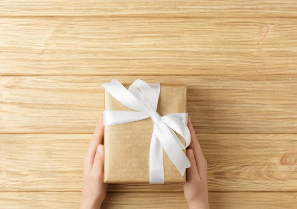 Ahşap arka plan üst görünümünde ellerde hediye kutusu — Stok fotoğraf