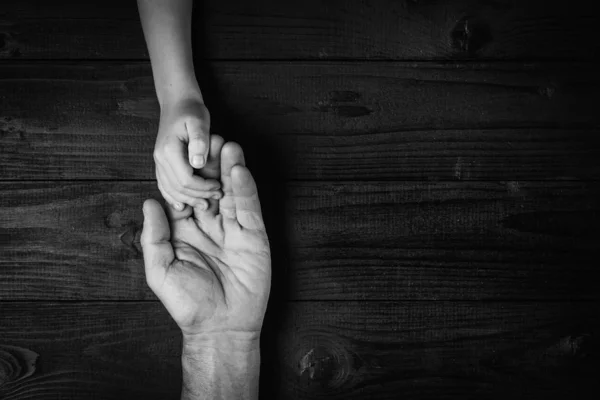 Erwachsene Hände, die Kinderhände halten, Familienhilfekonzept. Schwarz-weiß. — Stockfoto
