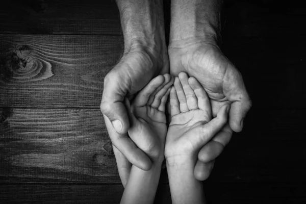 Mãos de um homem idoso segurando a mão de um homem mais jovem.. preto e branco . — Fotografia de Stock
