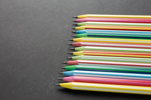 Lápices de colores en fila en una vista superior de fondo negro . — Foto de Stock