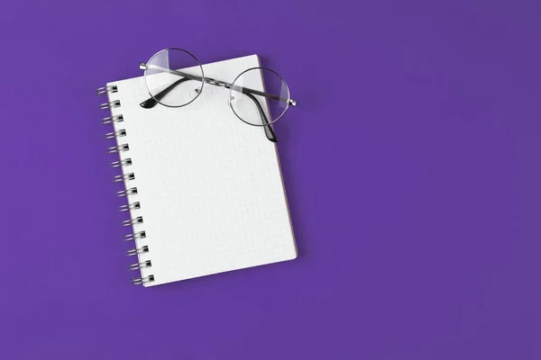 Notebook com óculos no fundo violeta — Fotografia de Stock