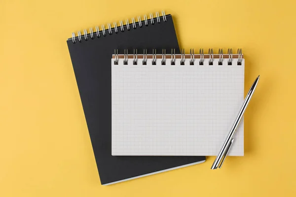 Школьные тетради с ручкой на желтом фоне — стоковое фото