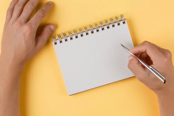 Dziewczyna pisze w otwartym notebooku widok z góry, żółte tło — Zdjęcie stockowe