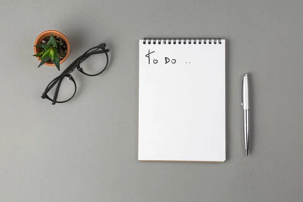 Notebook, pen, bril en groene bloem op een grijze achtergrond — Stockfoto