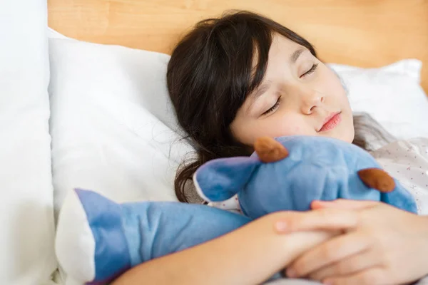 Дівчина спить з м'якою іграшкою на білому ліжку — стокове фото