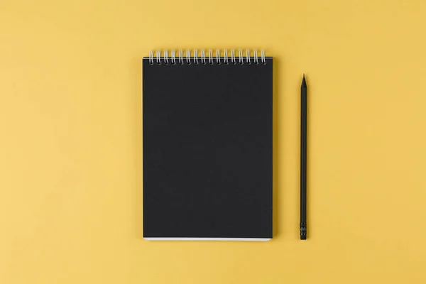notebook with black paper and pencil on a yellow background top view