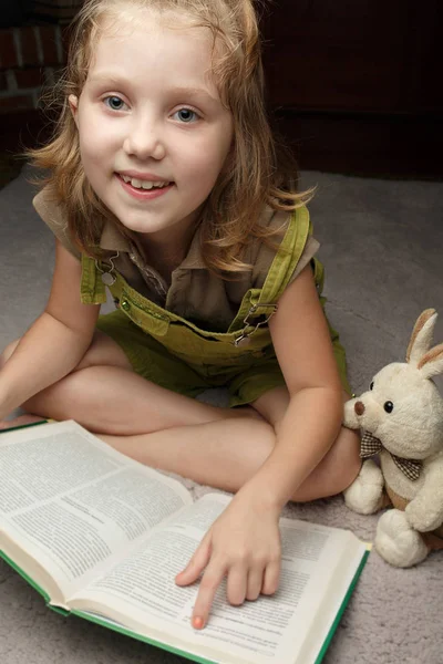 Mooi klein meisje lees boek met haar favoriete speelgoed — Stockfoto